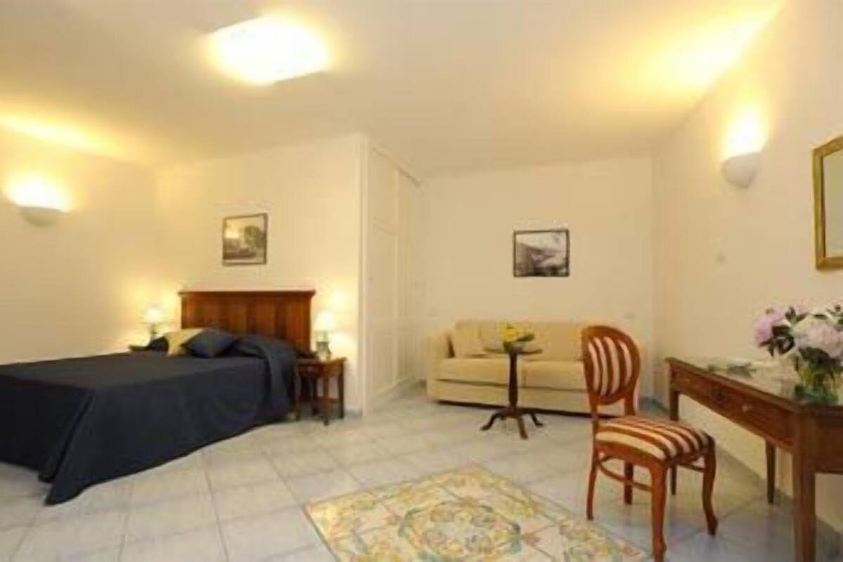 Un dormitorio con cama, escritorio, sillón, sofá y dos lámparas de pared.