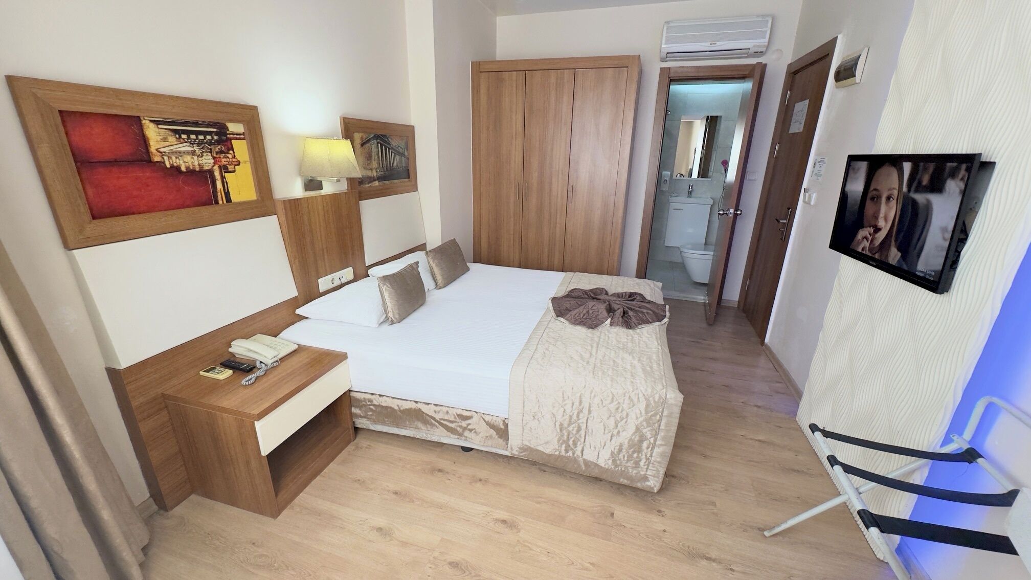 A hotel room with a bed, bedside table, lamp, wardrobe, and a TV mounted on the wall.