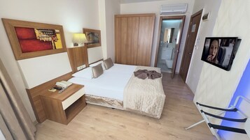 A hotel room with a bed, bedside table, lamp, wardrobe, and a TV mounted on the wall.