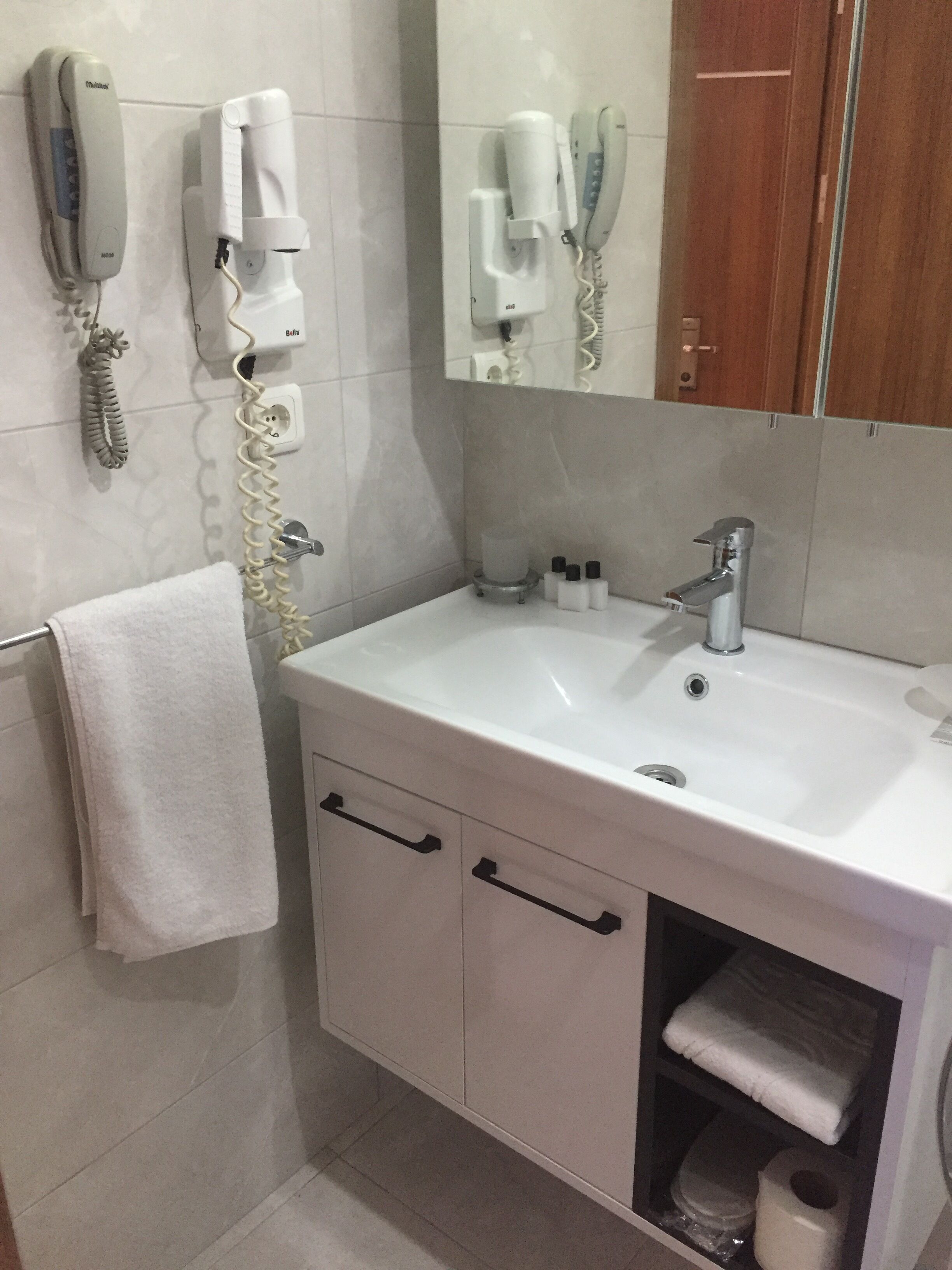 Une salle de bain avec un lavabo blanc, une serviette accrochée au mur et un miroir au-dessus du lavabo.