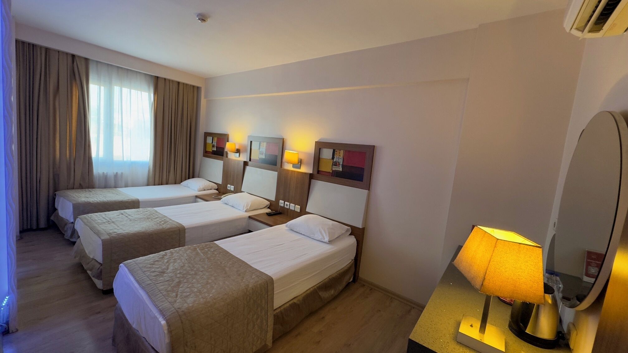 Quarto de hotel com duas camas de solteiro, uma mesa de cabeceira com abajur e um espelho grande.