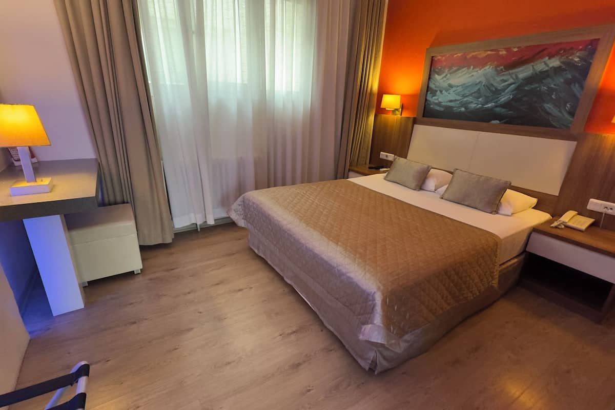 A hotel room with a large bed, bedside lamps, a desk, and a painting on the wall.