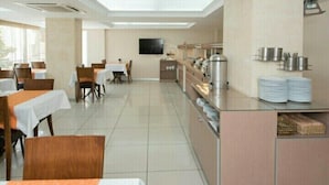 A spacious restaurant with multiple tables and chairs, a kitchen area, and a television mounted on the wall. - Hotel Baylan Izmir (Izmir)