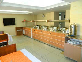 Habitación de hotel con barra de desayuno, televisor, reloj y cafetera.