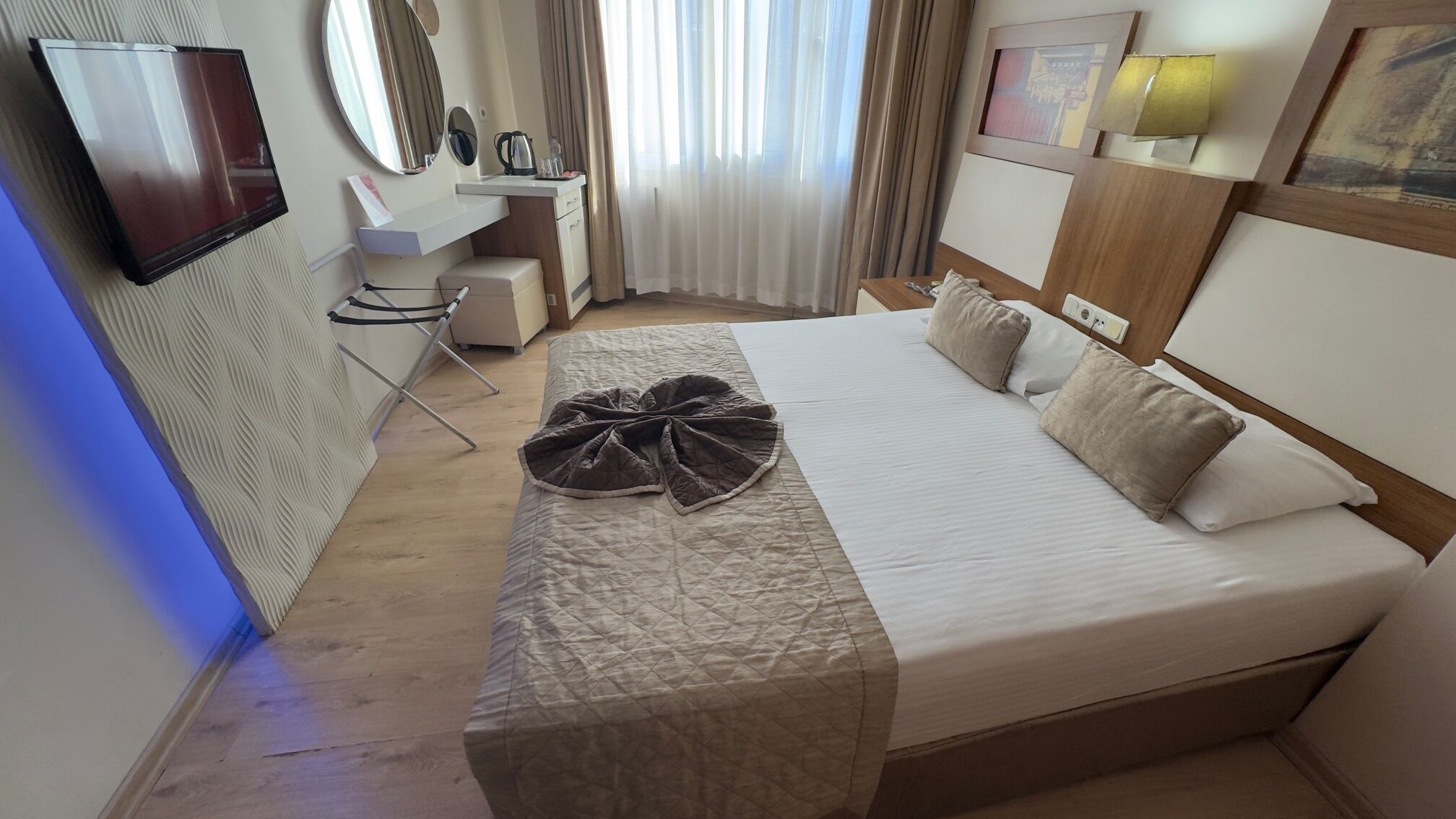 Habitació d'hotel amb un llit, escriptori, cadira, televisió i finestra amb cortines.