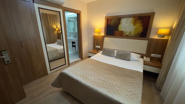 A hotel room with a bed, bedside lamps, a painting on the wall, and a mirror. - Hotel Baylan Izmir (Izmir)