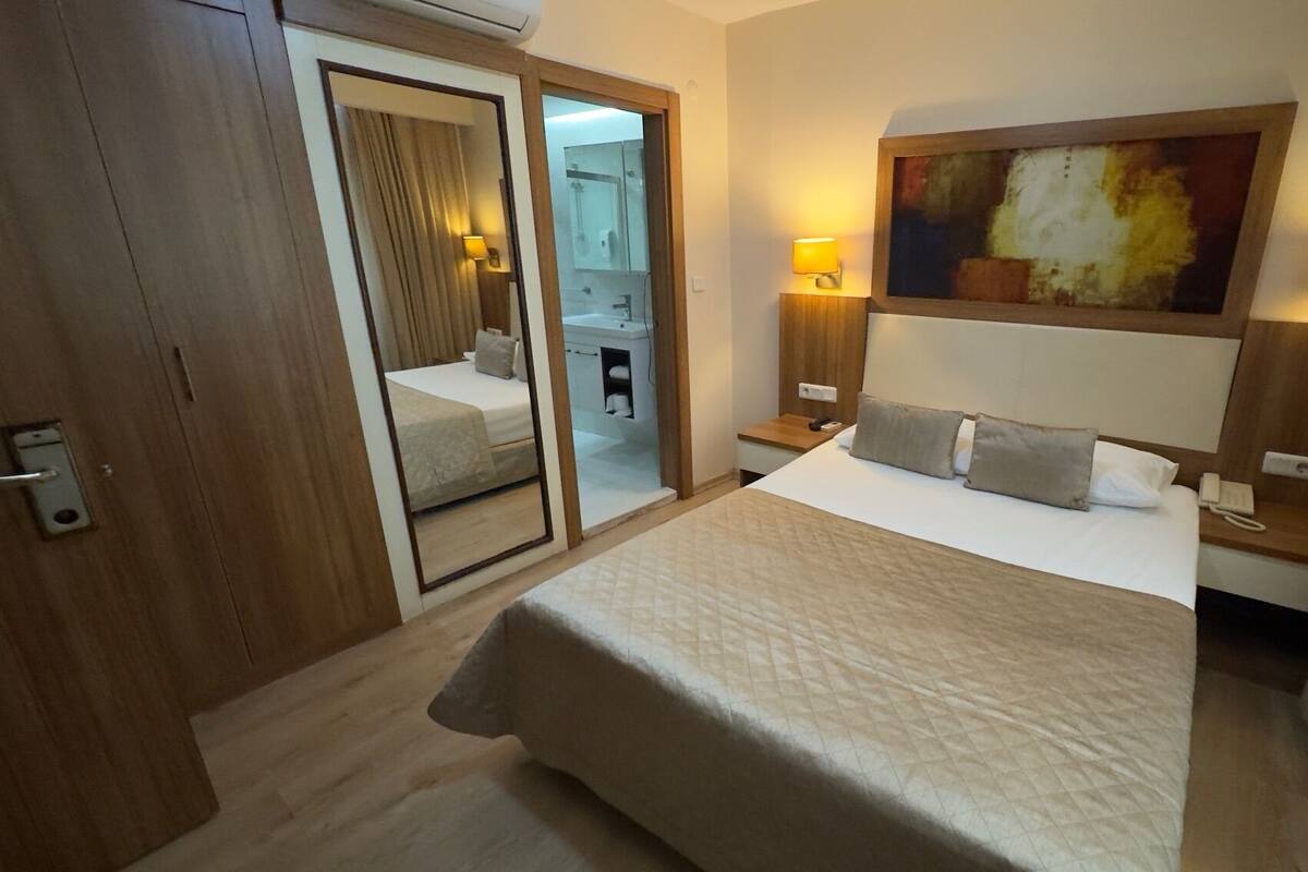 A hotel room with a bed, bedside lamps, a painting on the wall, and a mirror.