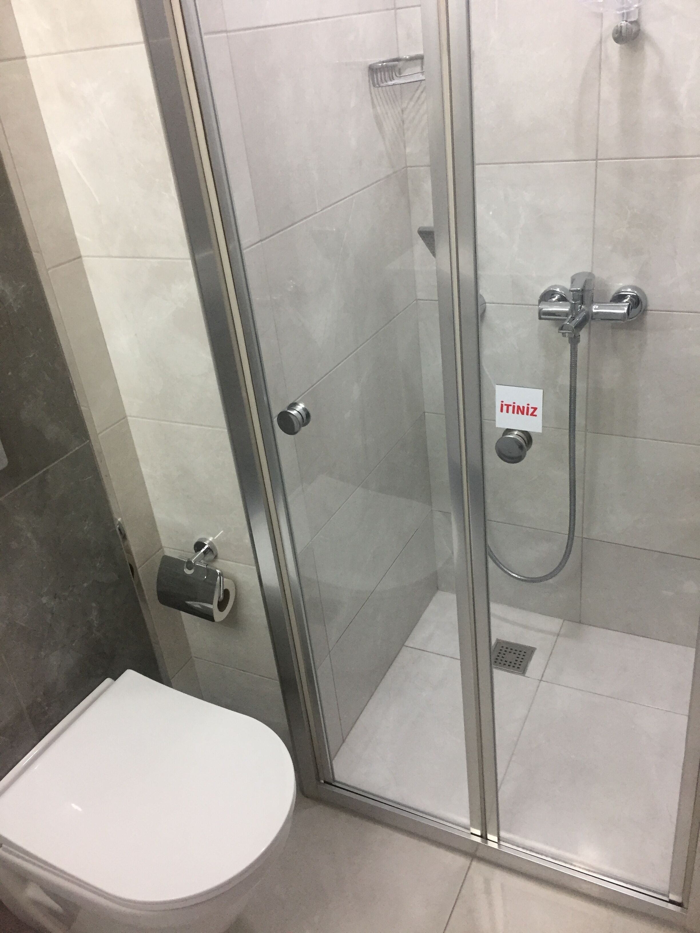 A bathroom with a glass-enclosed shower, a toilet, and a paper towel dispenser.