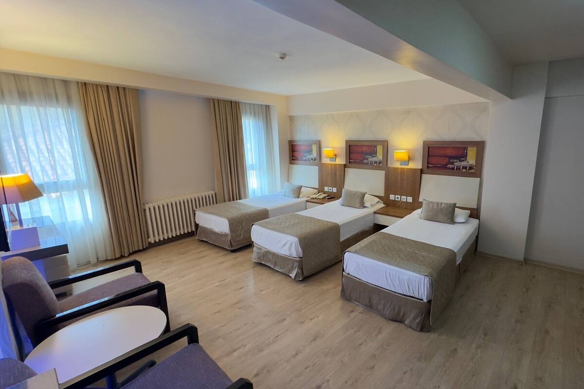 A hotel room with two single beds, a desk, a chair, and a radiator.
