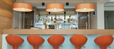 A bar area with orange bar stools and pendant lighting.