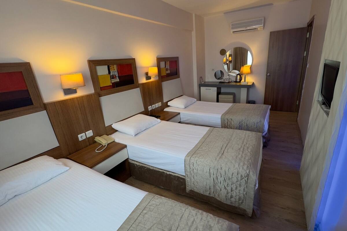 A hotel room with four single beds, a desk with a telephone, a mirror, and a television.