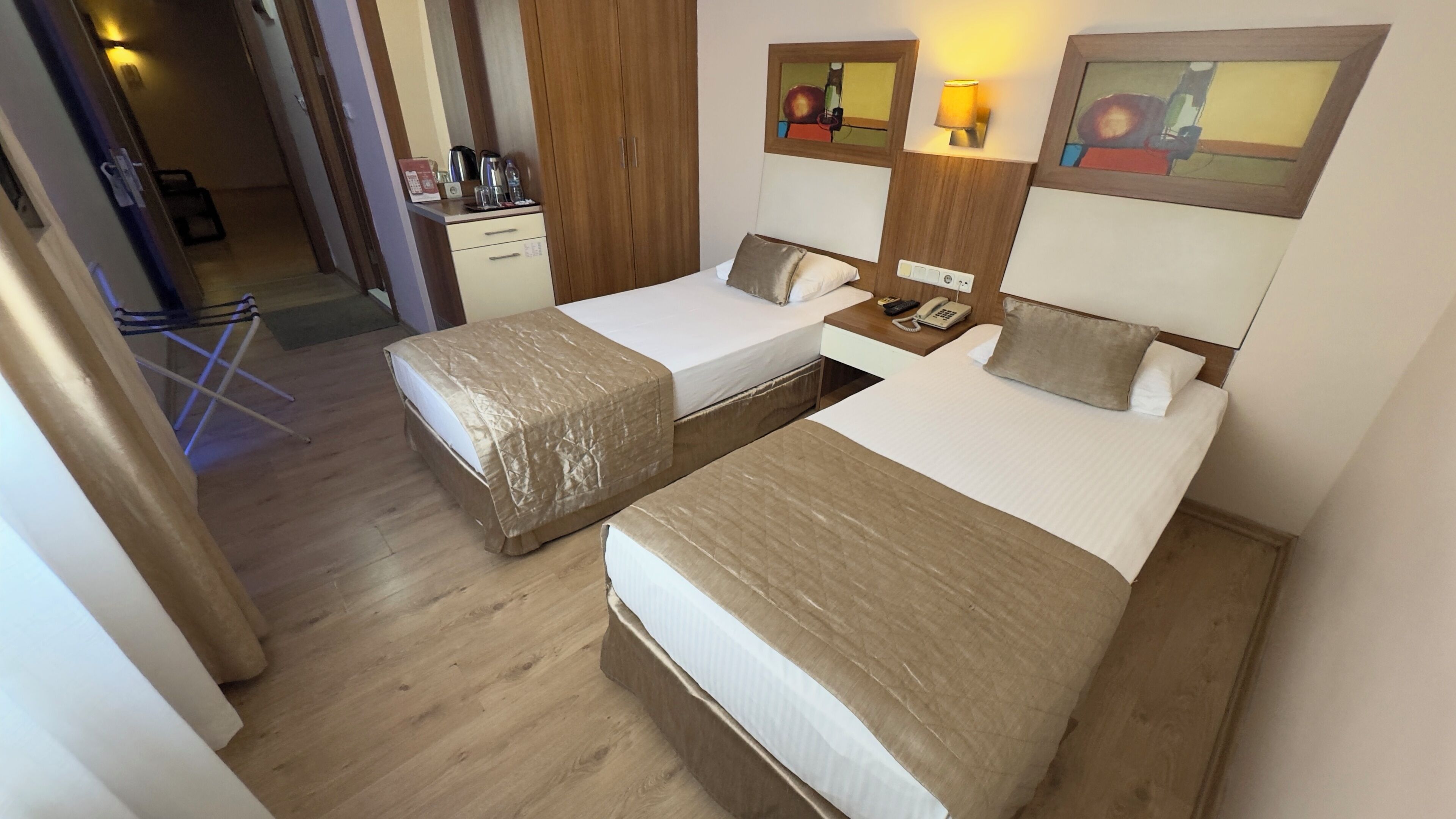 Habitación de hotel con dos camas individuales, piso de madera, un escritorio con teléfono y una kitchenette pequeña.