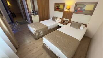 Habitación de hotel con dos camas individuales, piso de madera, un escritorio con teléfono y una kitchenette pequeña.