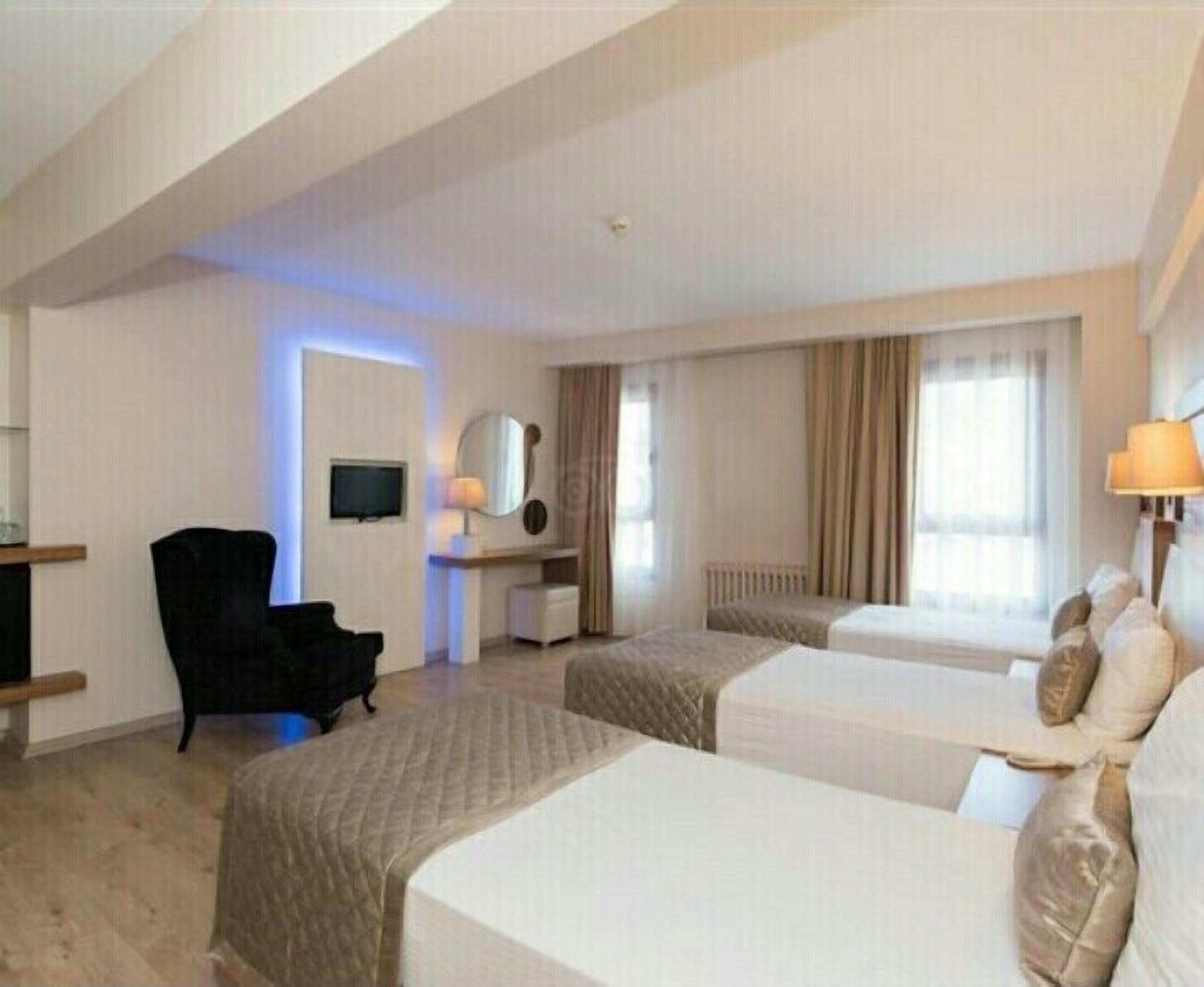 A hotel room with two beds, a desk with a chair, a TV, and a window with curtains.