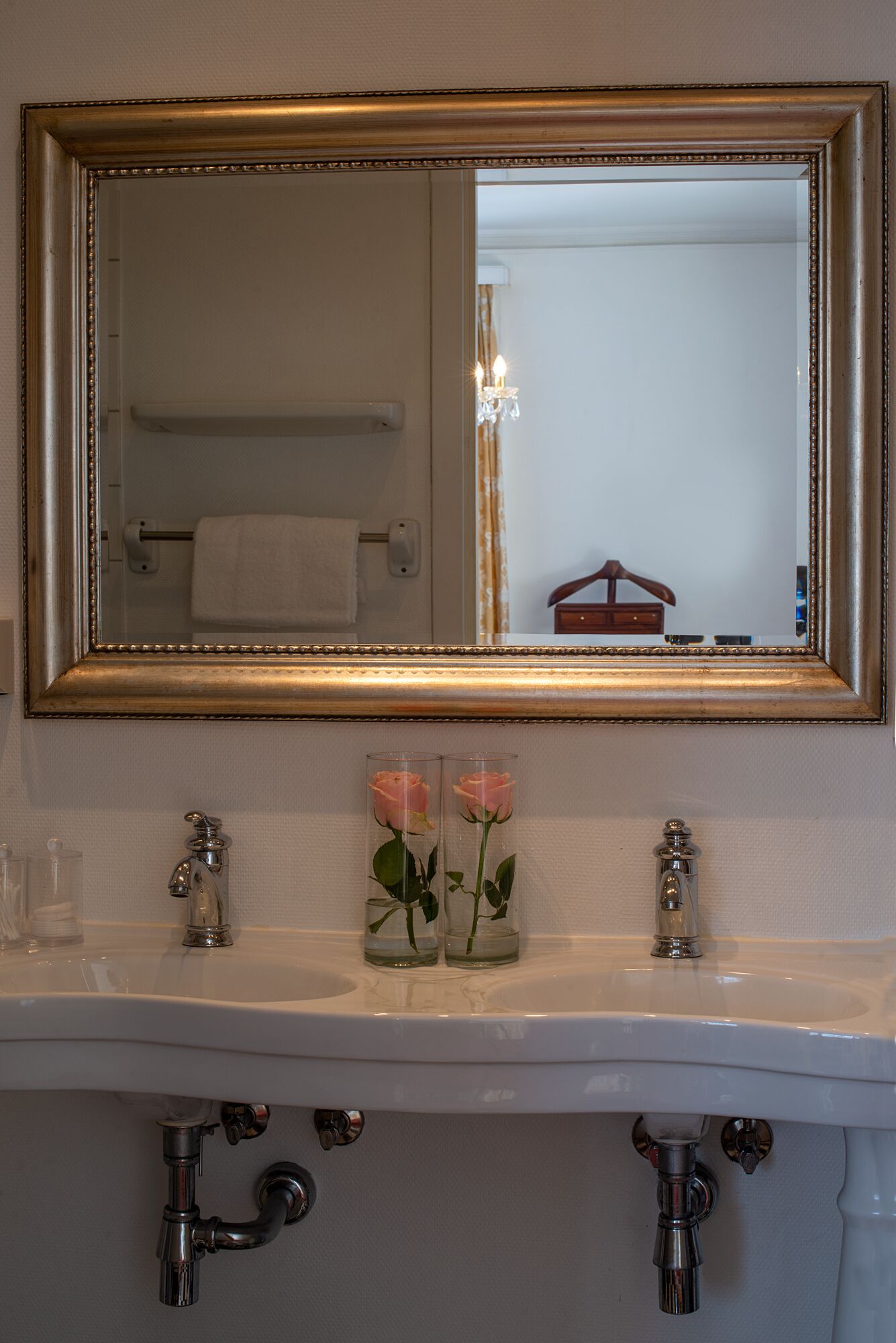 Un bagno con un grande specchio, due lavandini e due vasi di vetro con rose.