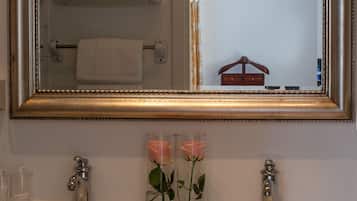 Un baño con un espejo grande, dos lavabos y dos jarrones de vidrio con rosas.
