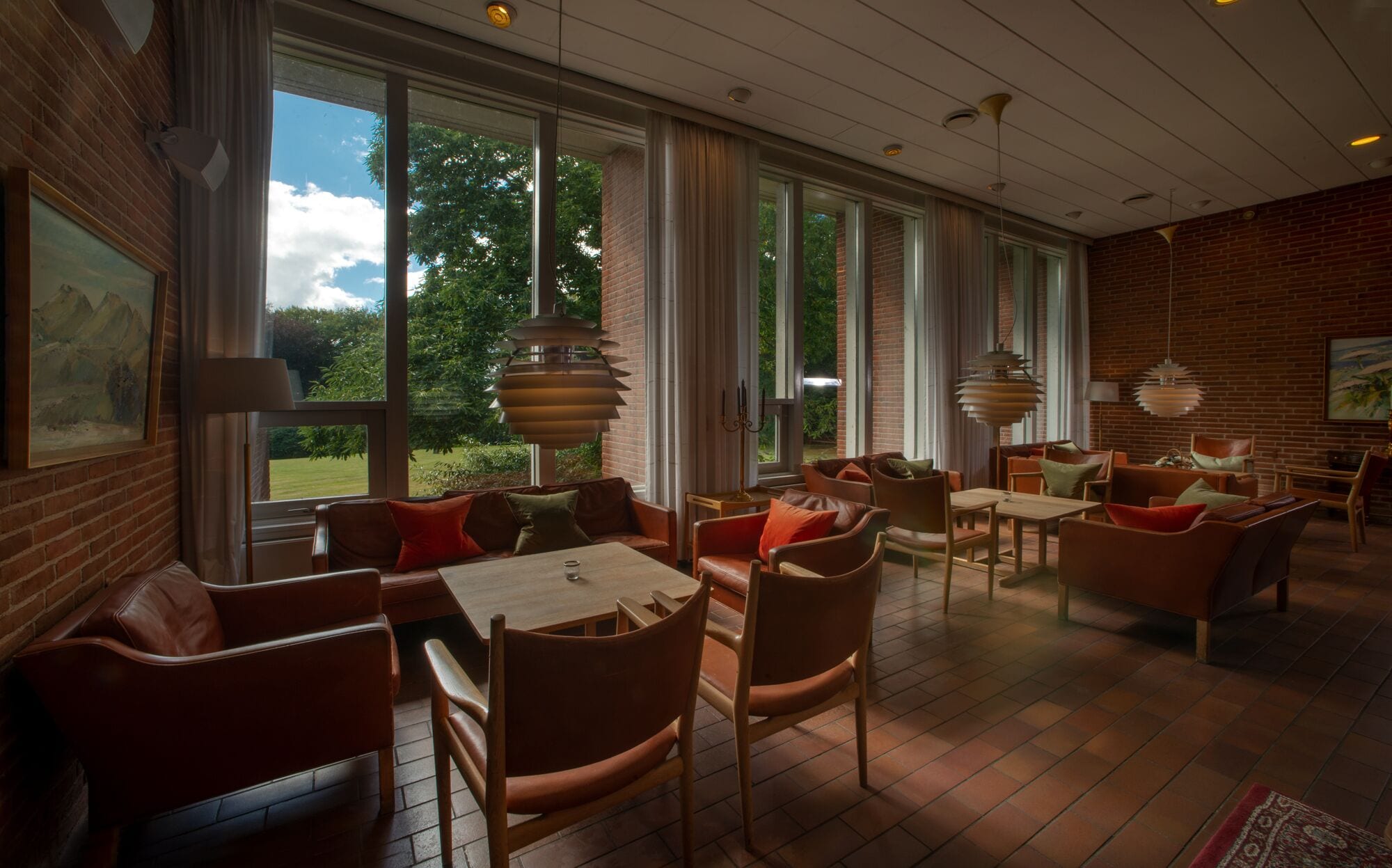 Een ruime kamer met grote ramen, lederen meubels en hangende lampen.