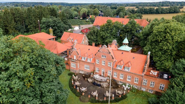 A large, historic building with a red-tiled roof, surrounded by lush greenery and a small pond. - Sauntehus Slotshotel (Hornbaek)