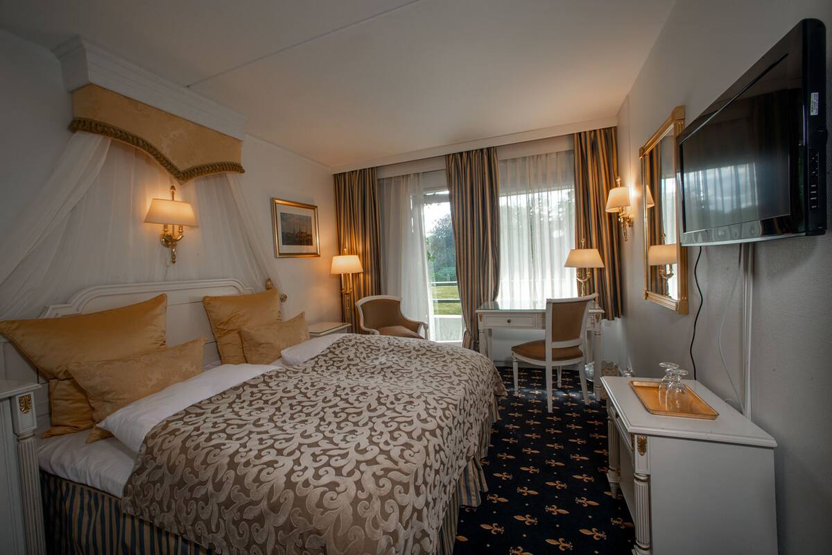 A hotel room with a large bed, a desk, a chair, a TV, and a window with curtains.