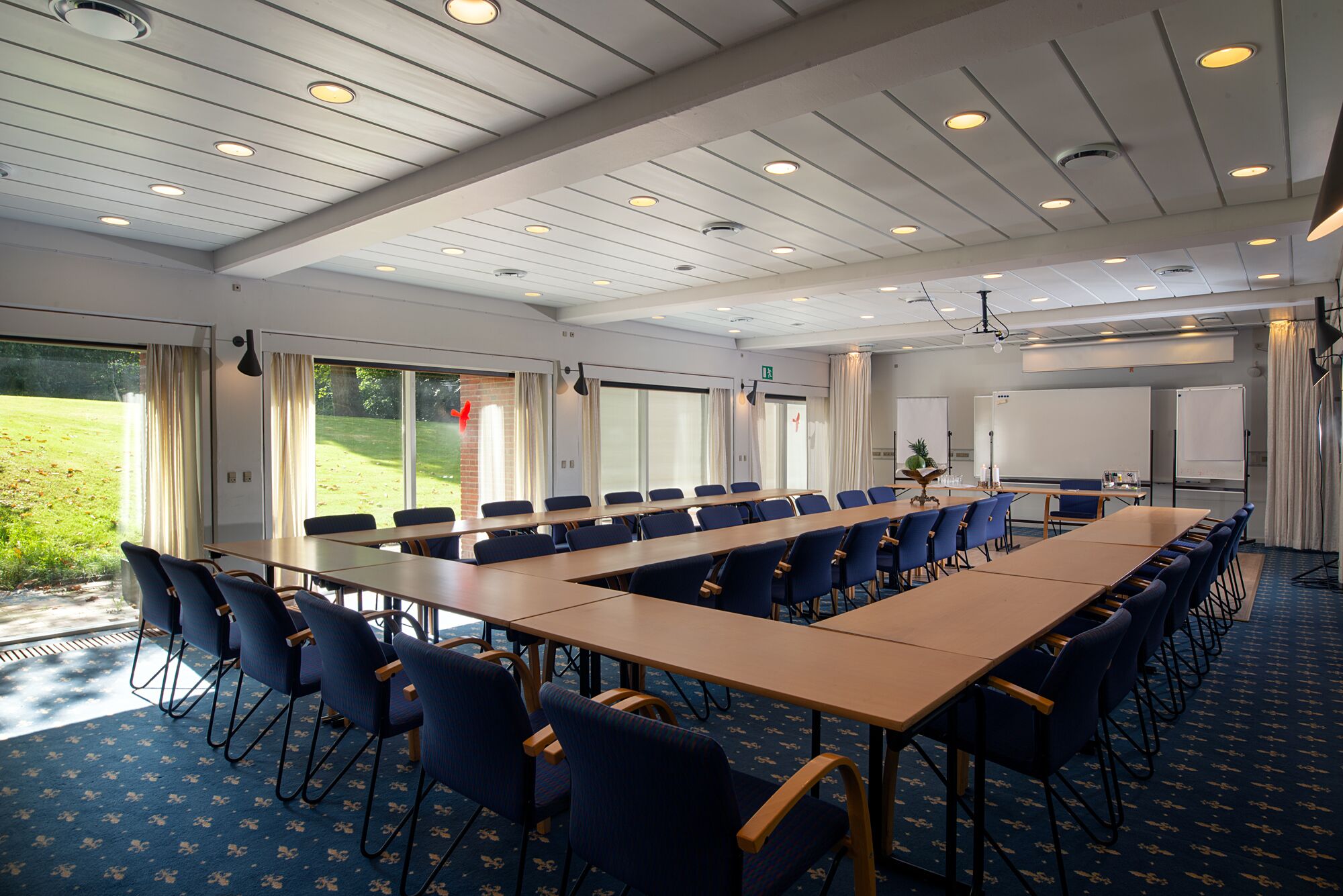 A conference room with a long table, blue chairs, and a view of a grassy area through large windows.