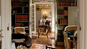 A dining area with a table set for six, surrounded by chairs. There is a bookshelf filled with books in the background. - Sauntehus Slotshotel (Hornbaek)