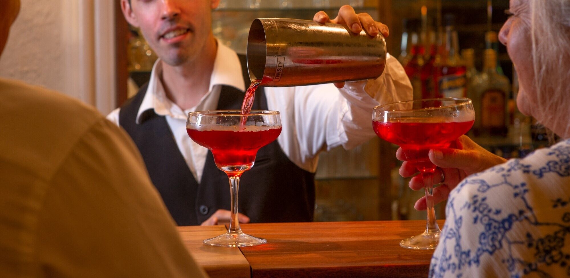 Un barman sirviendo una bebida roja en una copa de martini.