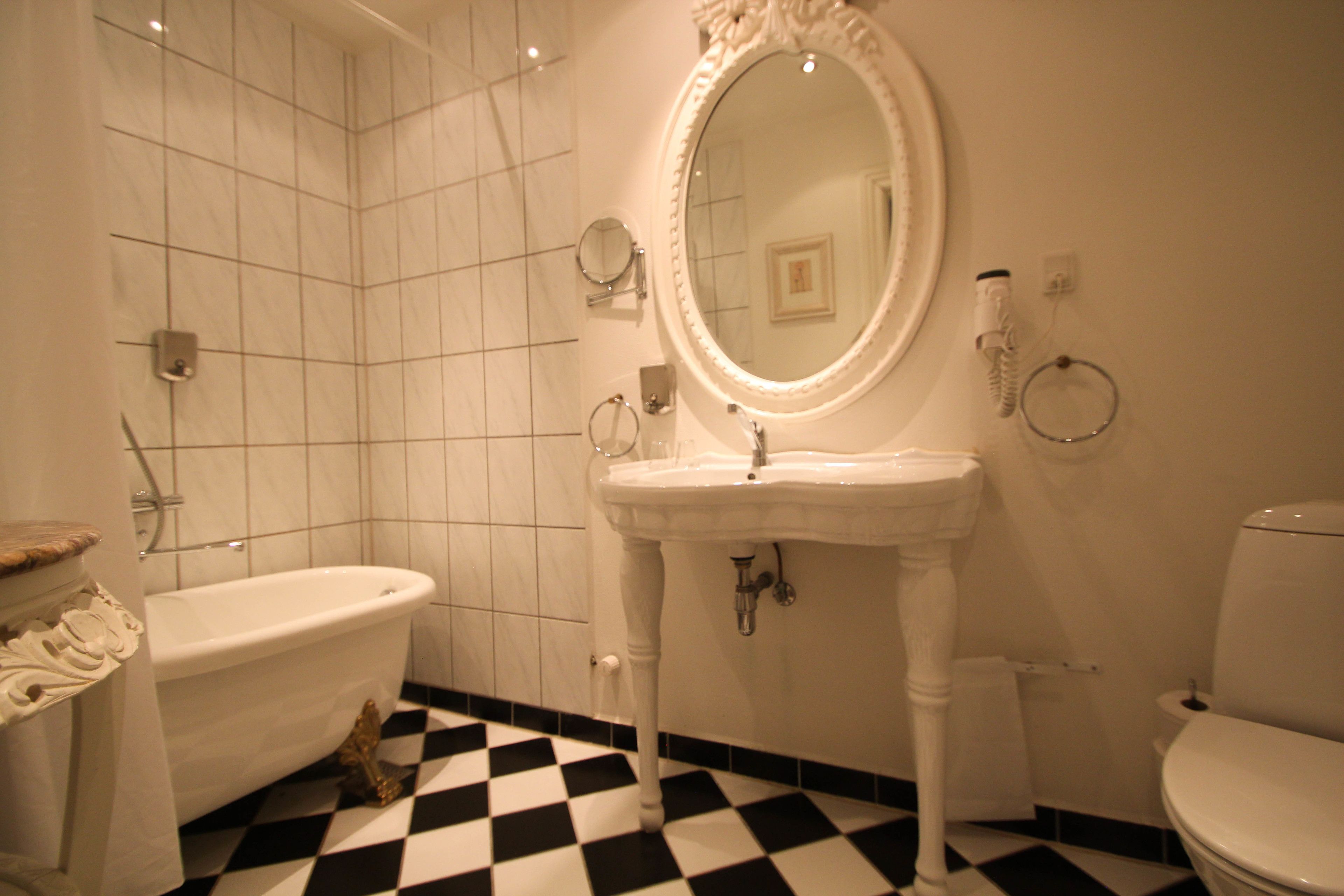 A bathroom with a white bathtub, a pedestal sink, a mirror, and a toilet.