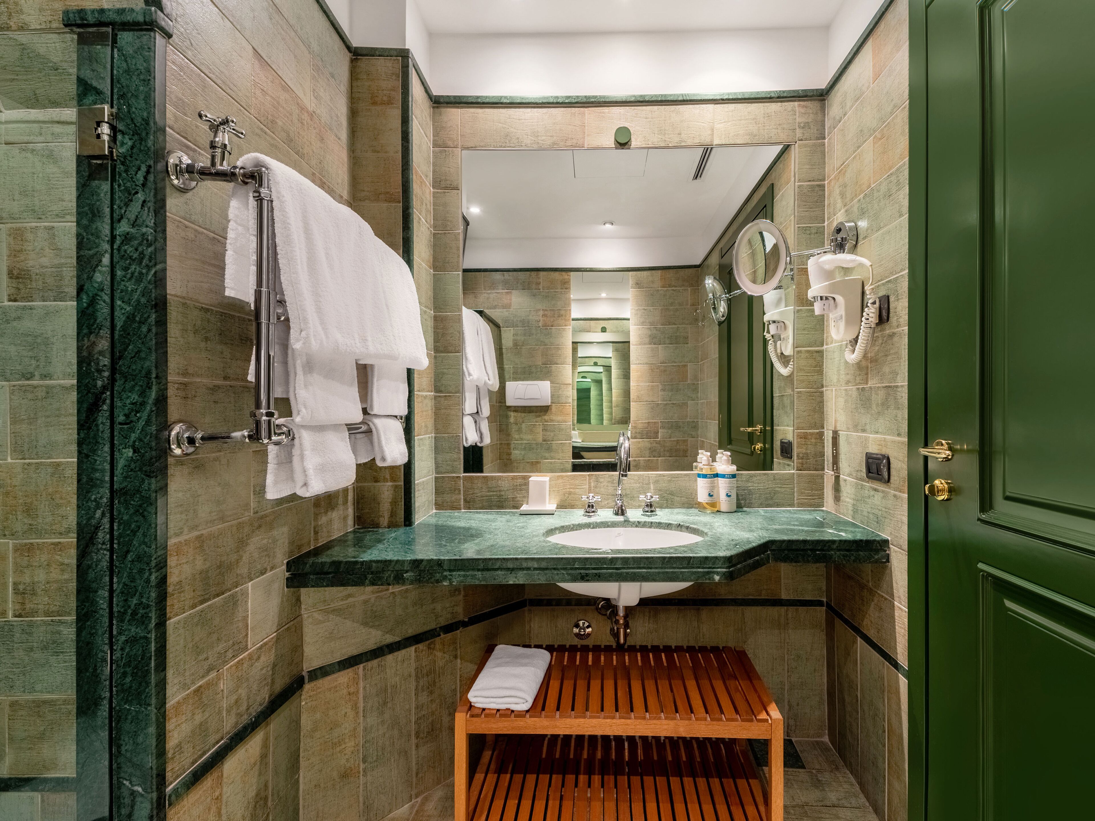 A bathroom with a marble sink, a wooden bench, and a green door.