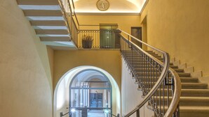 A grand staircase with ornate metal railings, leading to a balcony with a circular window and a clock. - Numa Milan Camperio (Milan)