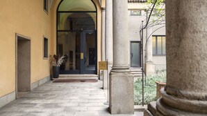 A corridor with stone columns, a yellow wall, and a door leading to a building. - Numa Milan Camperio (Milan)