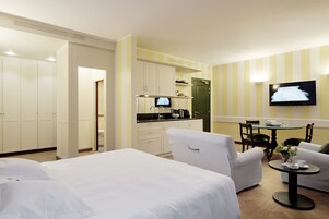 Ein Hotelzimmer mit Bett, einer Sitzecke mit Tisch, einem Fernseher und einer Küchenzeile.