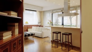 A modern living room with a white sofa, a wooden bookshelf, and two bar stools. - Numa Milan Camperio (Milan)