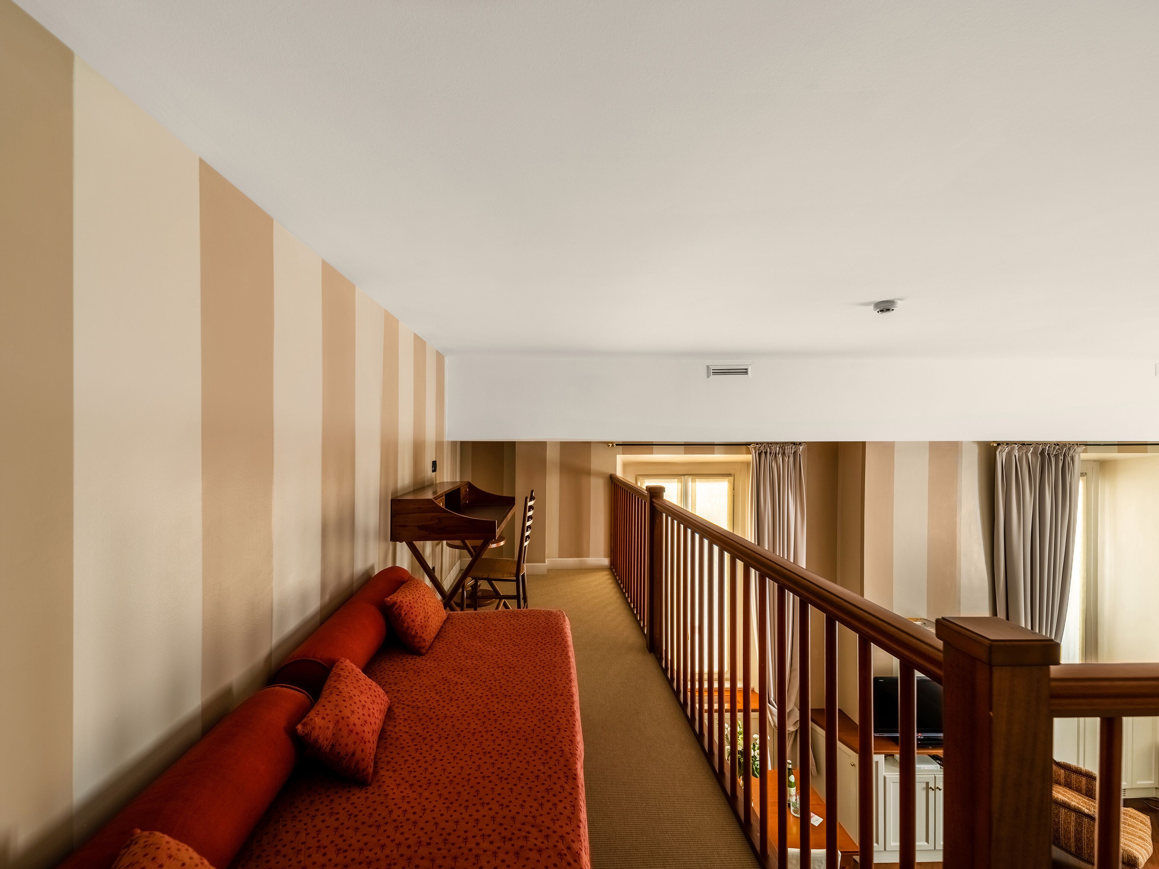A hotel room with a striped wall, a wooden desk, a red sofa, and a wooden staircase.