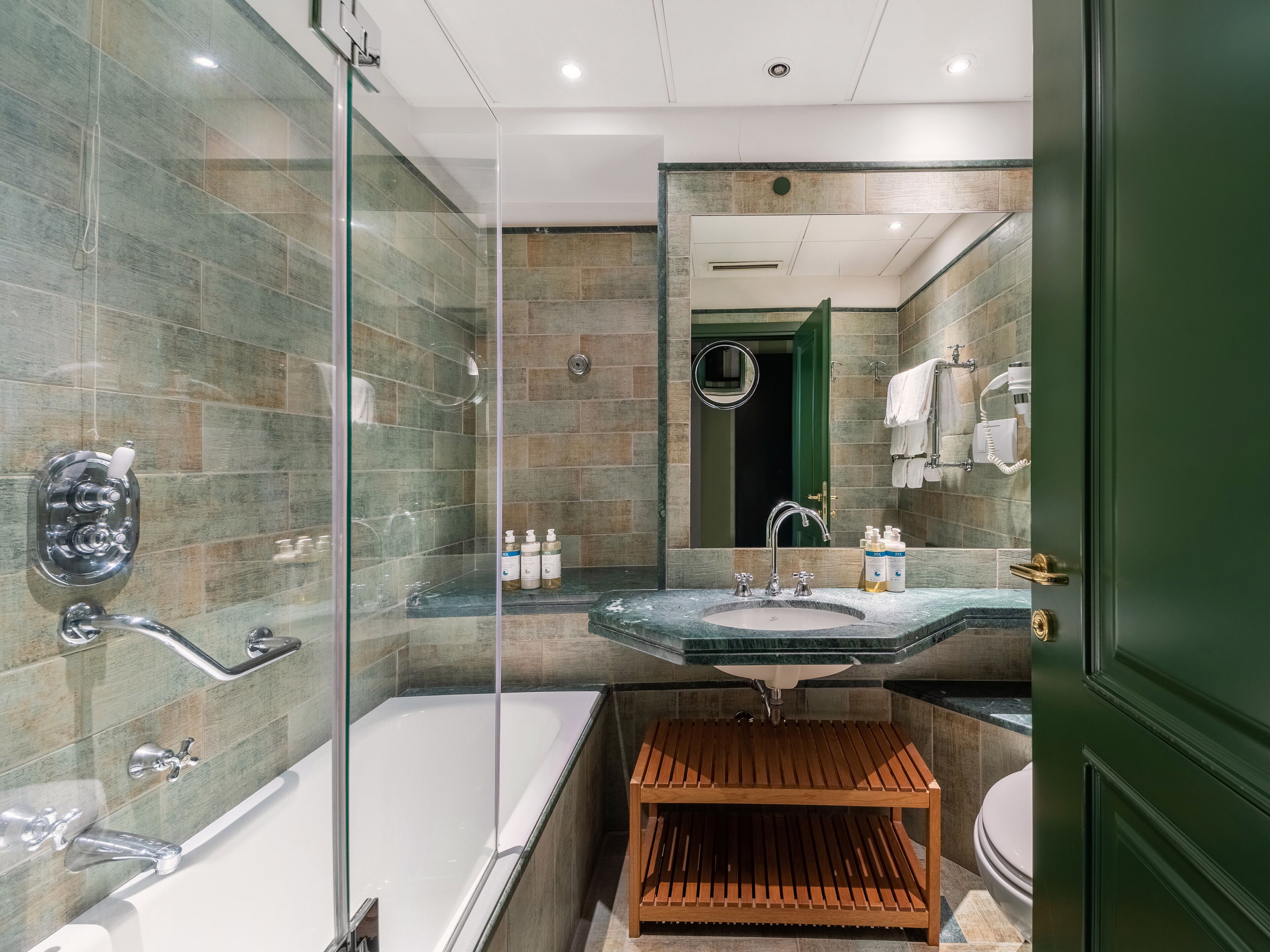 Un baño moderno con ducha envuelta en vidrio, una bañera independiente, un tocador con lavabo y un estante de madera.