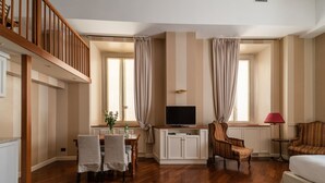 A spacious living room with wooden flooring, a dining area with a table and chairs, a television, and two armchairs. - Numa Milan Camperio (Milan)