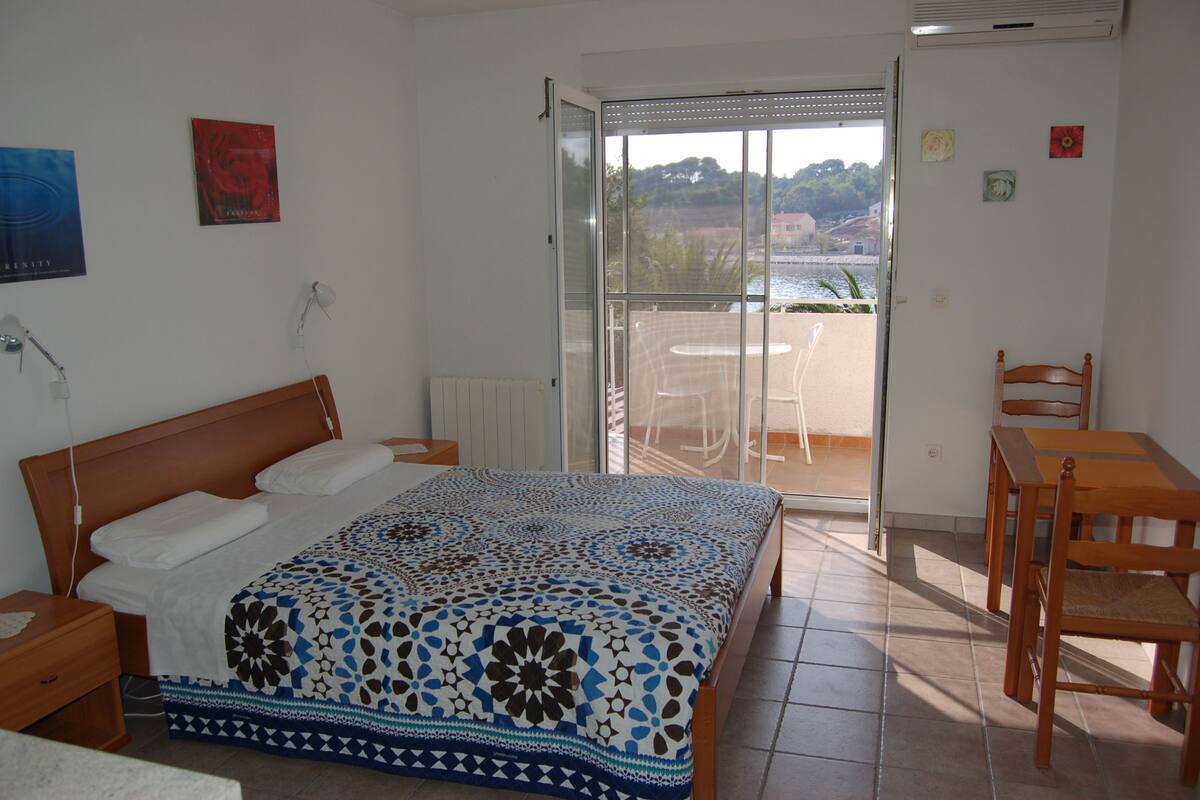Une chambre avec un lit, une table de chevet, une chaise en bois, une table et un balcon donnant sur l’eau.