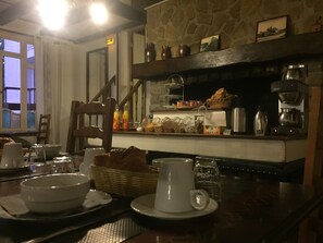 A breakfast bar with a stone fireplace, wooden chairs, and a variety of breakfast items. - Auberge du Moulin d'Audenfort Guest House (Clerques)