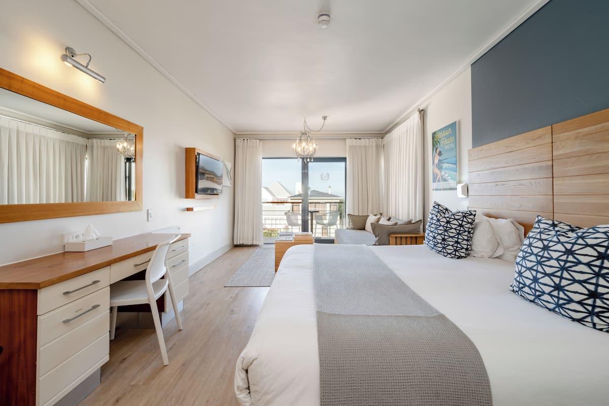 Habitación de hotel moderna con un escritorio de madera, una cama grande con almohadas estampadas, un espejo grande y vistas al exterior.