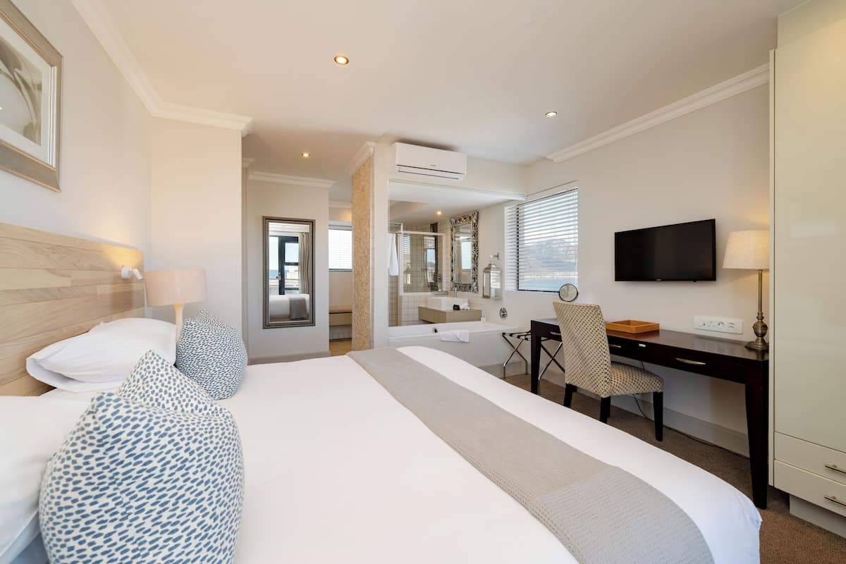 Habitación de hotel con una cama grande, un escritorio, una silla, un televisor y un baño visible a través de una puerta abierta.