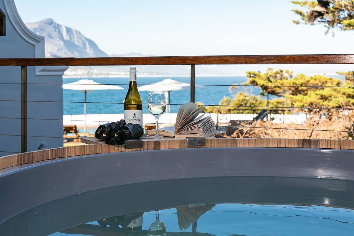 Tinaco con una botella y una copa de vino, una cámara y un libro abierto, con vistas a un paisaje marino.