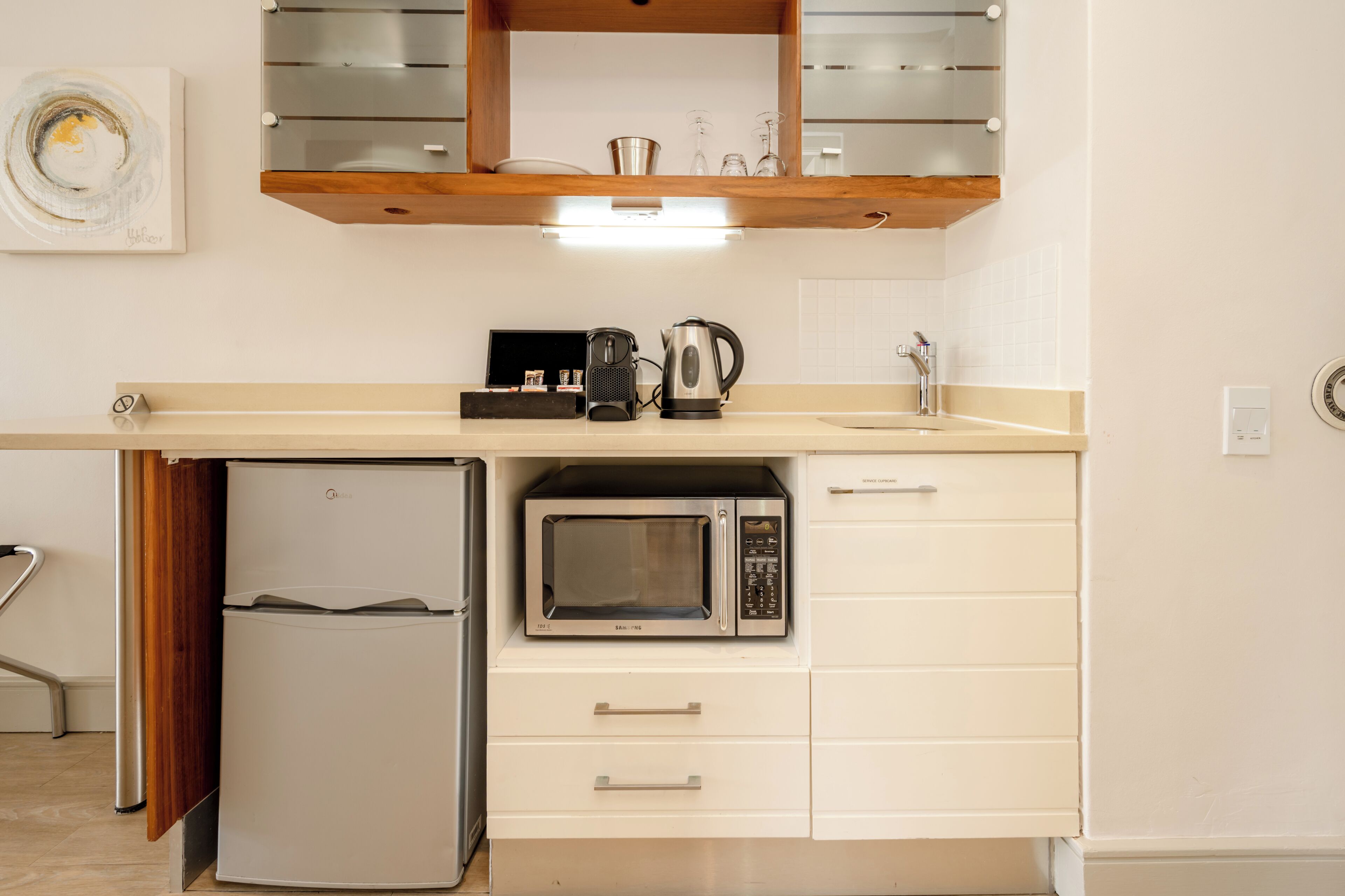 Una cocina compacta con microondas integrado, cafetera y refrigerador pequeño.