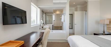Habitación de hotel con cama, escritorio con bandeja, silla, televisor, bañera y espejo.