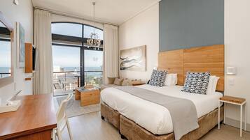 A modern hotel room with a large bed, a desk, and a balcony with a view.