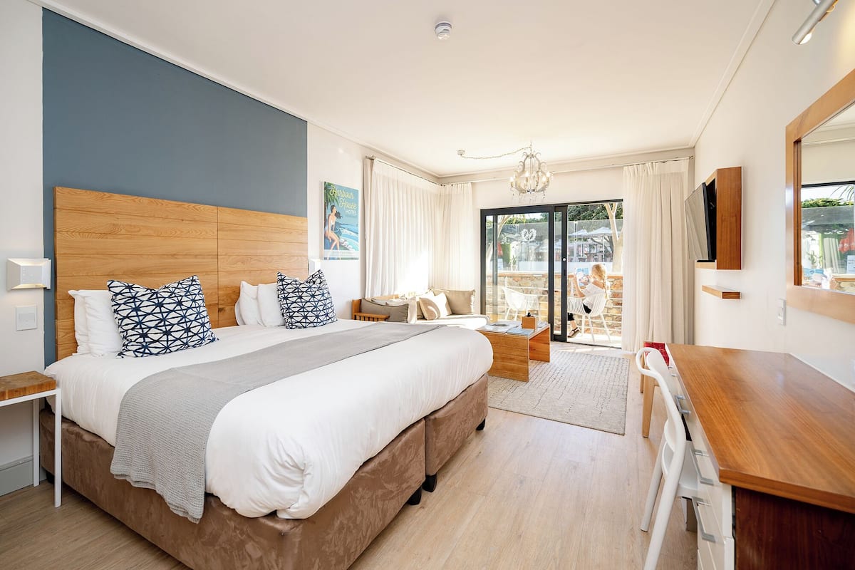 Una habitación de hotel moderna con una cama grande, cabecera de madera, escritorio y balcón con vistas.