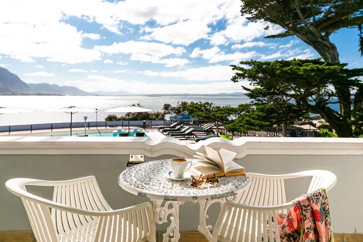 Una terraza con una mesa, sillas y vistas a una piscina y montañas.