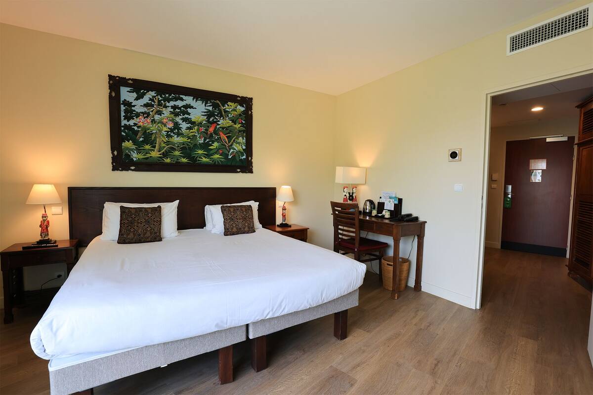 Habitación de hotel con una cama grande, dos mesitas de noche con lámparas, un escritorio con silla y un cuadro en la pared.