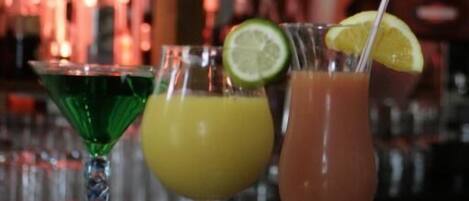 Drei Cocktails auf einer Bar, im Hintergrund unscharf Regale mit Flaschen.