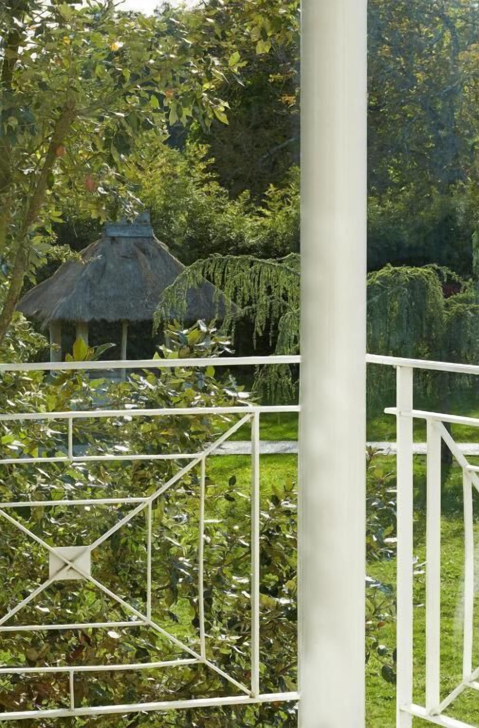A garden with a thatched-roof structure, surrounded by lush greenery and a white metal fence.