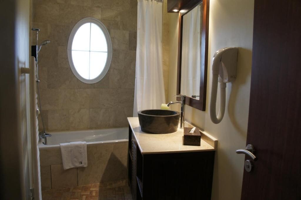 A bathroom with a bathtub, a round window, a sink with a basin, and a mirror.