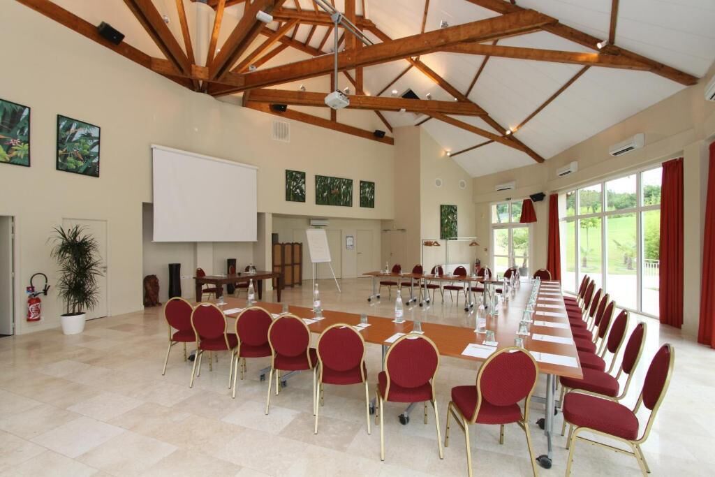 Une salle de conférence avec une longue table, des chaises rouges et un tableau blanc.